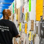 man in black crew neck t-shirt standing beside yellow and white wall